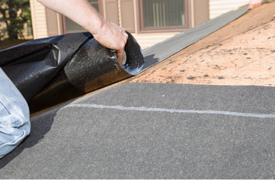 A worker is laying black synthetic underlayment on the roof.